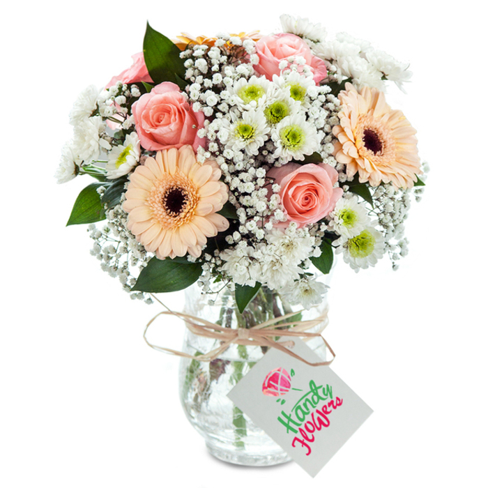 Set against a luminous white background, this elegant bouquet-crafted in Rush Green and exuding the care of a seasoned local florist-displays a sophisticated medley of pastel blooms. The arrangement's focal point is a trio of classic, peach-tinted roses whose layers of velvet-soft petals open gracefully, each expressing a quiet romance that would feel at home on a sunlit table near Crow Lane. Flanked by bright peach-orange gerbera daisies with pronounced dark centres, the bouquet radiates joy, while plump spray chrysanthemums in crisp white, some boasting fresh lime-green centres, add texture and dimension. Intertwined throughout are delicate clusters of baby's breath, their fine white blossoms creating a cloud-like fullness reminiscent of early morning mist rolling through Rush Green's community gardens. The bouquet is punctuated with sprigs of deep green eucalyptus, adding refreshing structure and a subtle aromatic note that invites you closer. These fresh-cut stems are gathered in a clear, textured glass vase, showcasing the water and natural arrangement below; a piece of rustic raffia encircles the neck in a gentle bow, holding a blank white tag ready for a heartfelt message. Whether gracing a home on Birkbeck Road or offered as a gift to celebrate life's milestones, this bouquet is both timeless and distinctly local, an emblem of Rush Green's warmth and floral artistry-ready for convenient flower delivery throughout the area.
